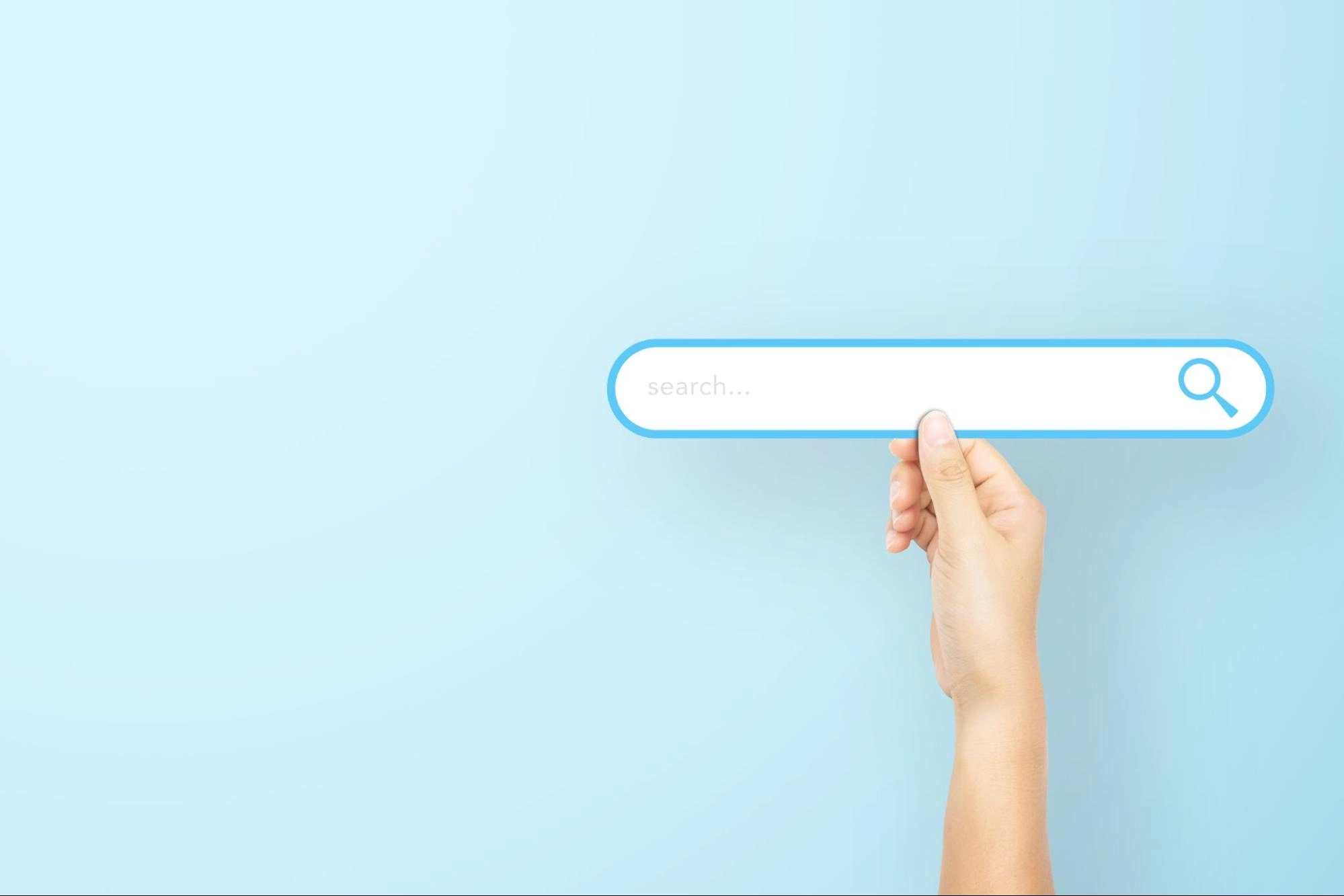 Hand holding a stylized search bar icon on a light blue background, representing online search and SEO services.